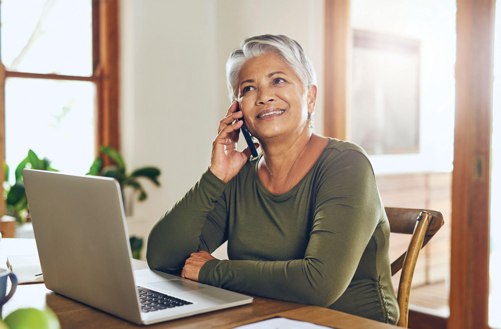 Senior woman talking on her phone while sitting in front of your laptop.