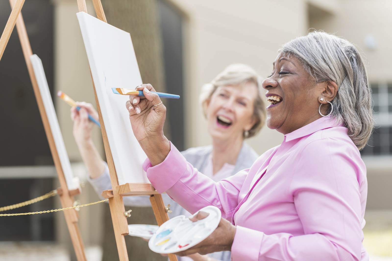 Two multi-ethnic senior women painting pictures on canvases.